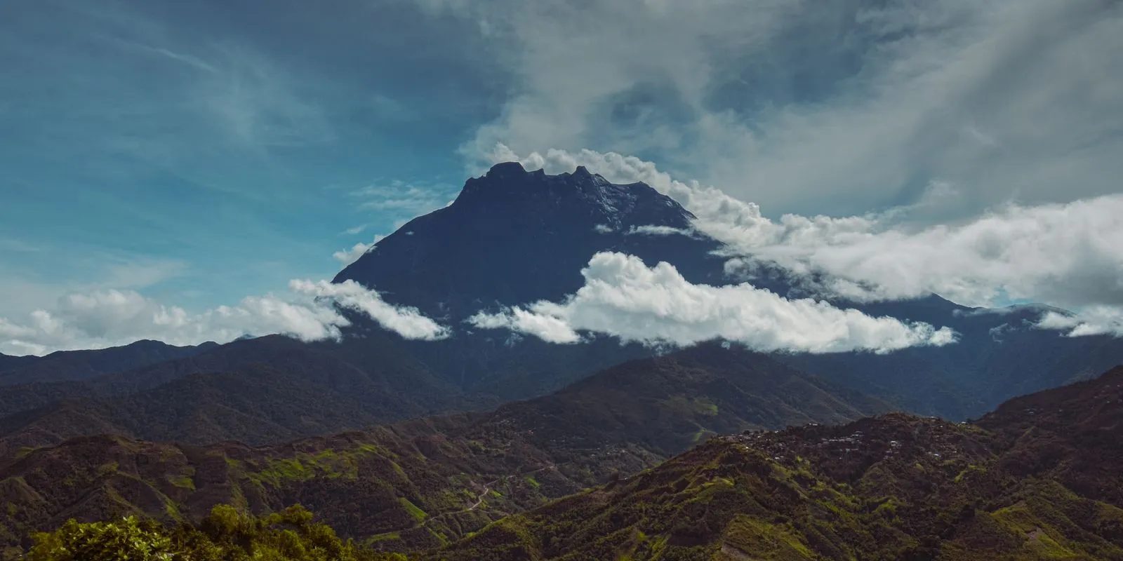 Mount Kinabalu wrapped in cloud above the hills around Kundasang