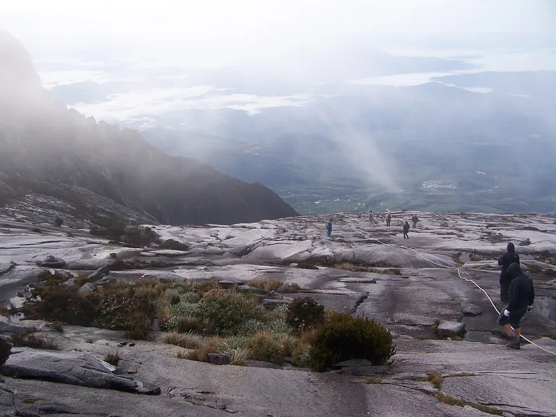 Climbers crossing the granite summit plateau of Mount Kinabalu in morning mist