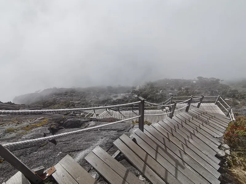 Wooden boardwalk with rope rails on misty granite slopes of Mount Kinabalu
